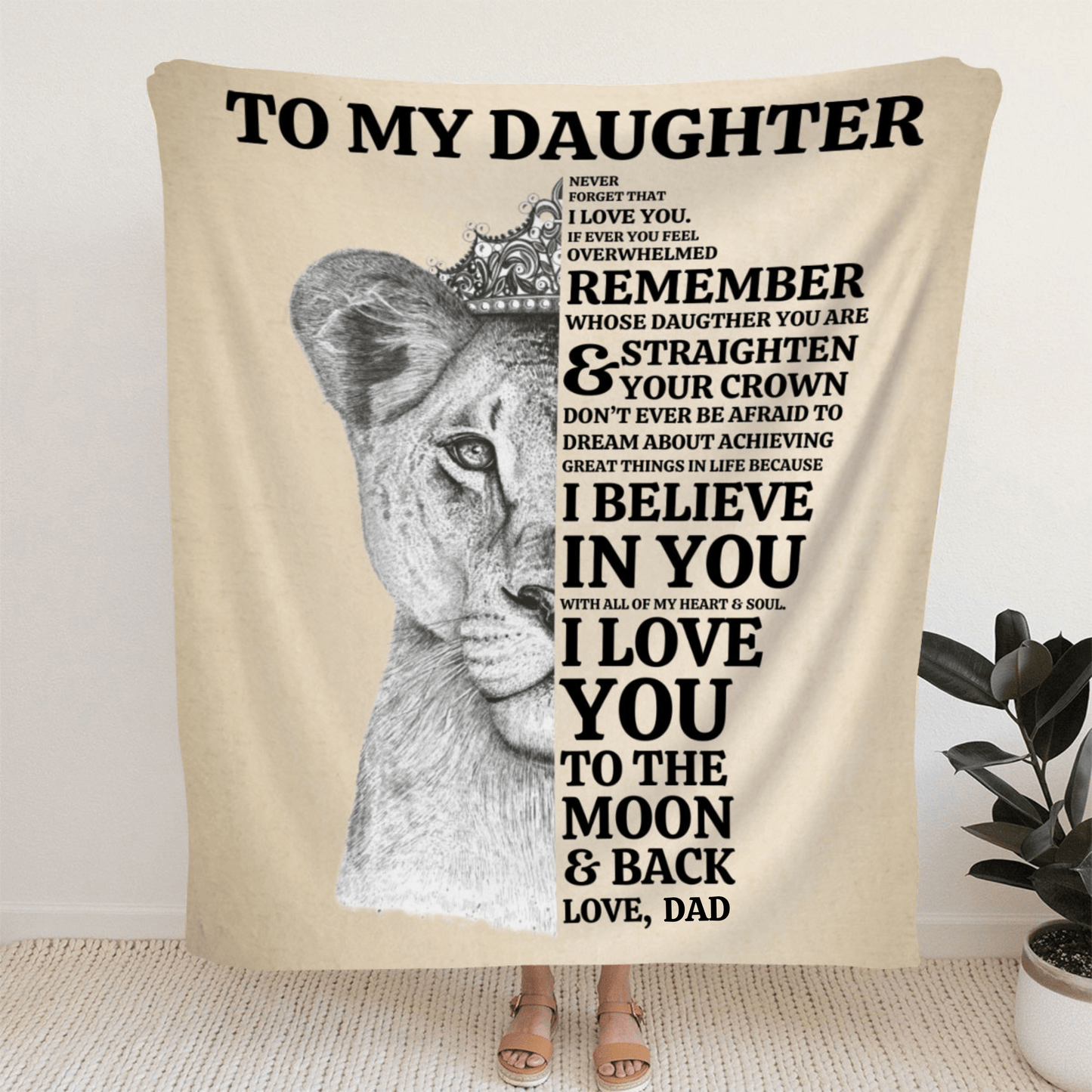 A woman standing holding a tan blanket with a lioness face on it with a message from mom to daughter that says always remember whose daughter you are and straighten your crown. I believe in you and I love you to the moon and back.