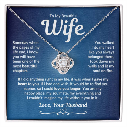 A necklace with a love knot pendant and cubic zirconia, presented in a box with a message to wife, set against a blue background.