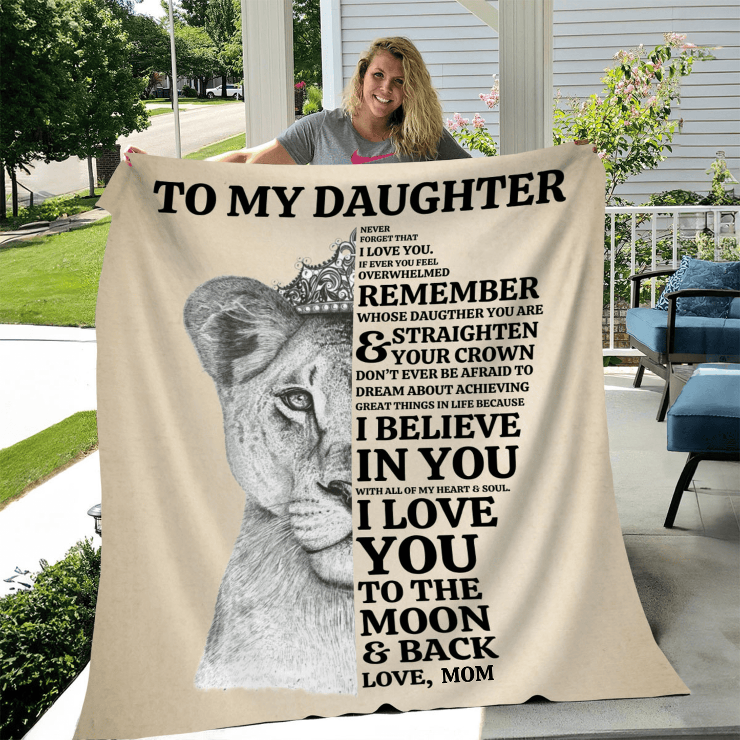 I woman standing holding a tan blanket with a lioness face on it with a message from mom to daughter that says always remember whose daughter you are and straighten your crown. I believe in you and I love you to the moon and back.